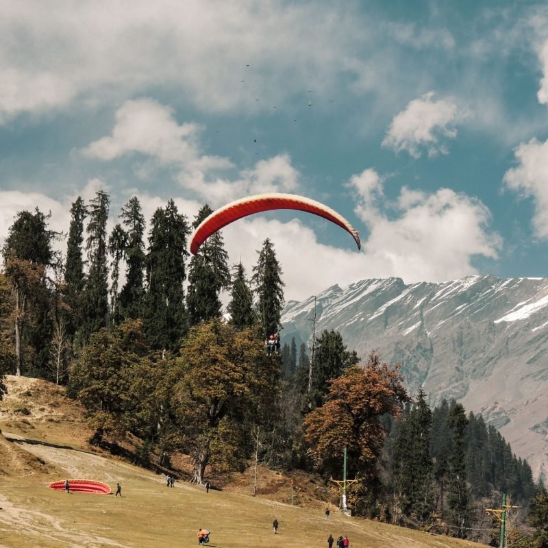 Thrilling paragliding above Manali's scenic landscape with majestic Himalayan mountains.